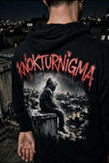 Black hoodie with a large back print of a hooded figure sitting on a rooftop ledge overlooking glowing city lights, dark graffiti stencil style, with KNOKTURNIGMA in large arched red graffiti letters across the upper back.